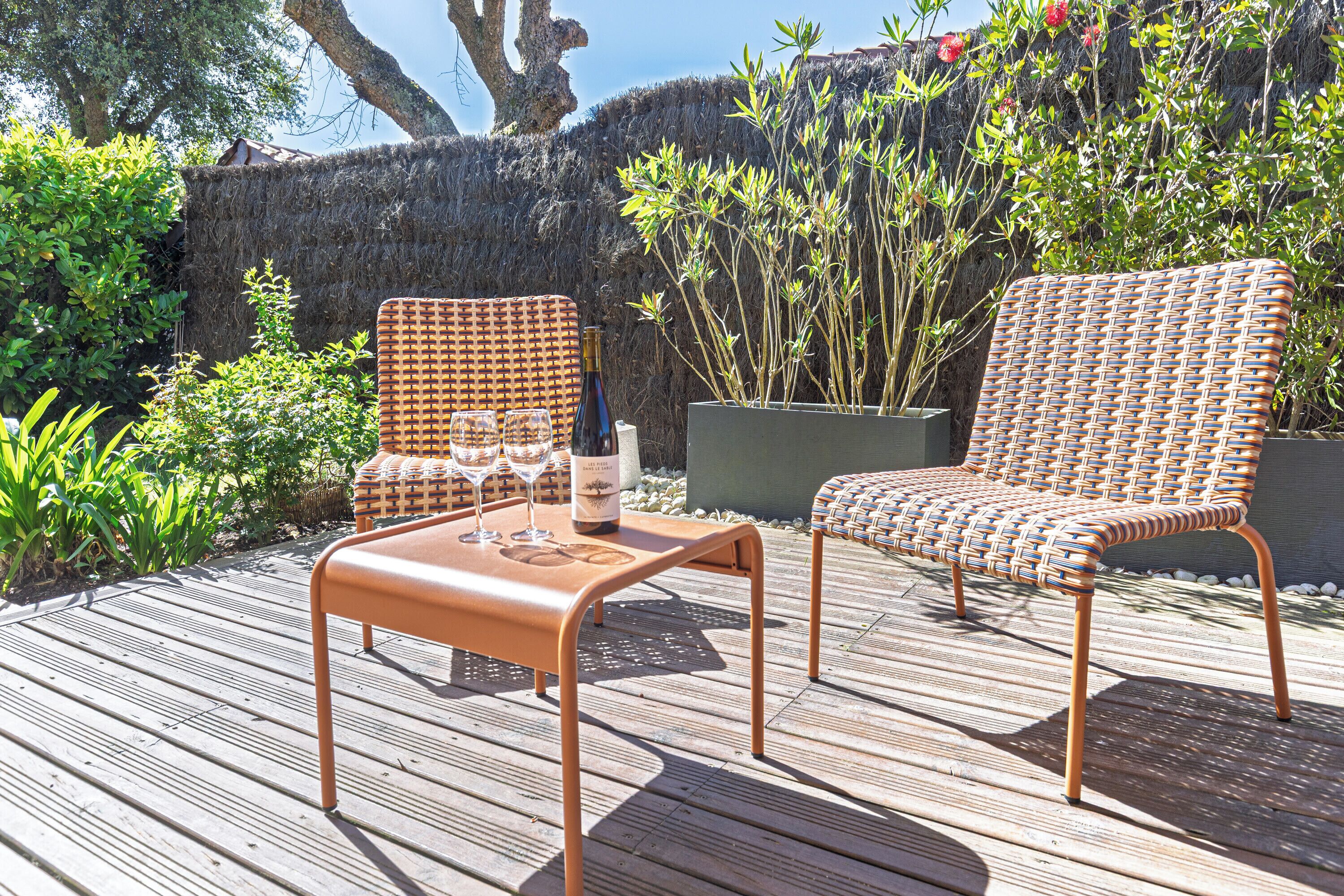 Een houten terras met twee rieten stoelen en een tafel, een fles en glazen.