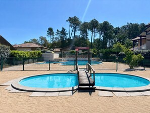 A swimming pool with a wooden deck and a lifeguard stand, surrounded by a fence and trees. - Villa Le Bosquet aux Écureuils - Welkeys (Capbreton)