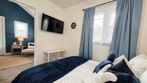 Un dormitorio con cama, televisión montada en la pared, escritorio y silla.