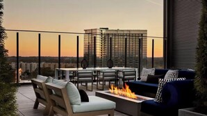 An outdoor terrace with a fire pit, seating, and a view of a cityscape at sunset. - Modern Luxury 1BR Skyline Views + Pool (Atlanta)