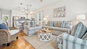 A spacious living area with a sofa, armchairs, a coffee table, and a kitchen in the background.