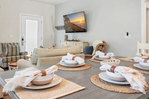 A dining area with round tables set with bowls and placemats, a sofa, and a TV mounted on the wall.