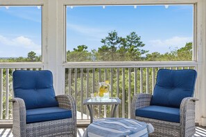 A covered outdoor seating area with wicker furniture and a glass table with a drink.