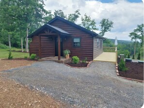 A log cabin with a porch, a gravel driveway, and a wooden deck.