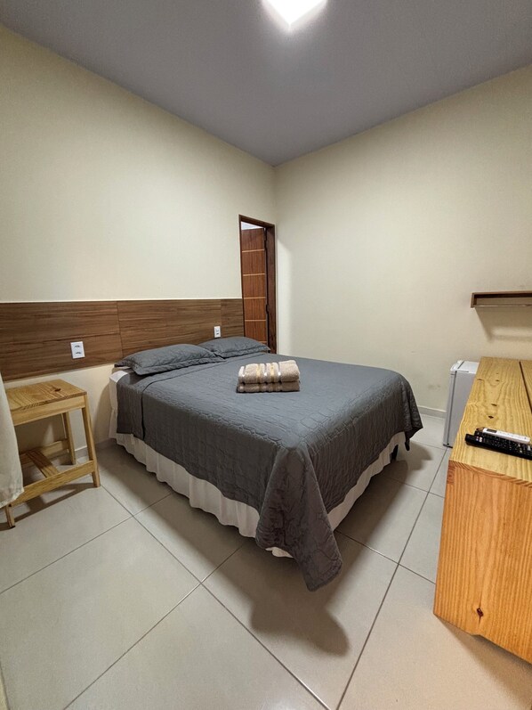A bedroom with a bed, a wooden nightstand, a desk, and a wardrobe.
