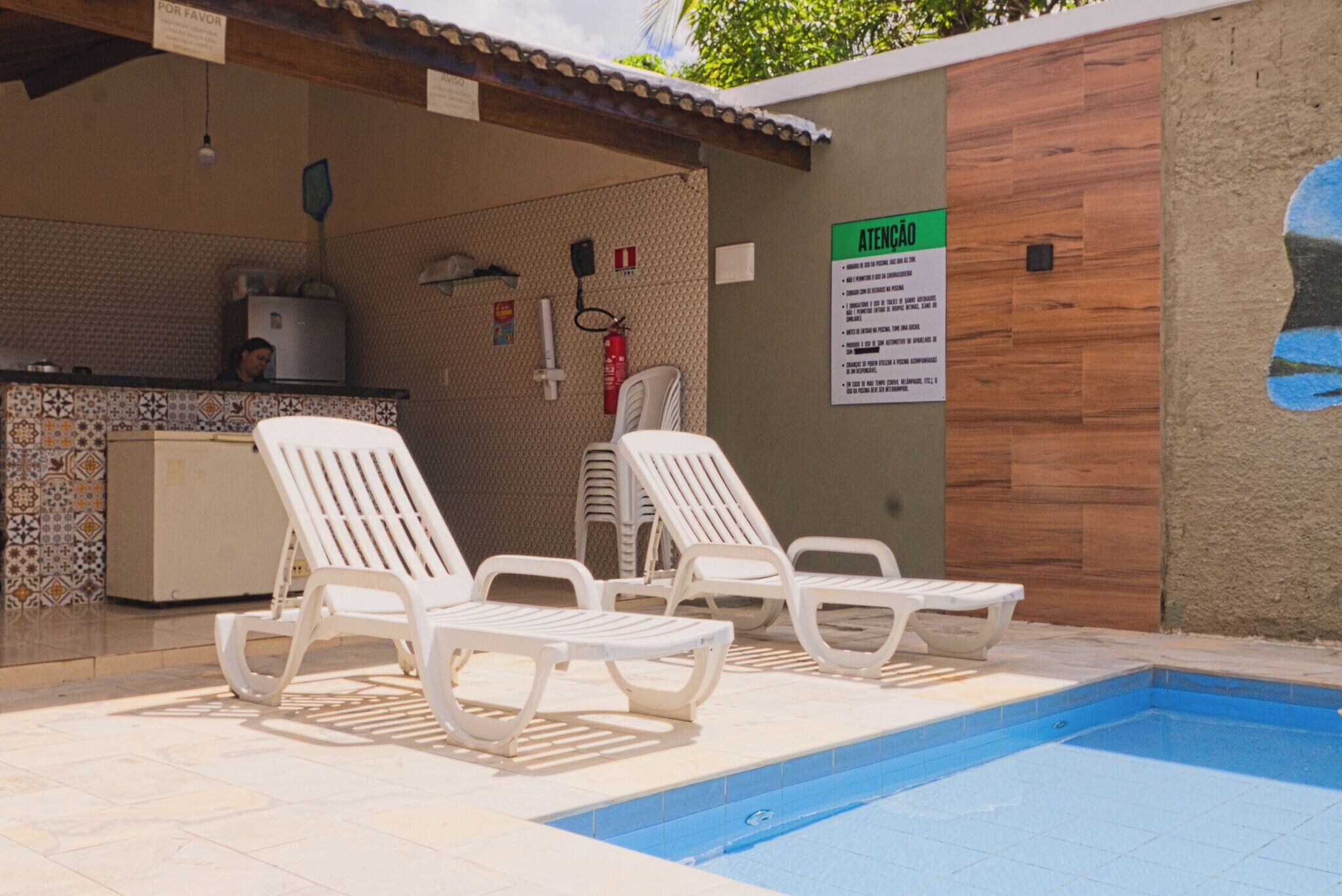 Zona de piscina con sillas de descanso y un cartel.