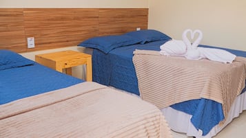 Habitación de hotel con tres camas, cada una con un edredón de diferente color, un cabecero de madera y una mesita de noche de madera.