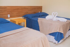 A hotel room with three beds, each with a different colored blanket, a wooden headboard, and a small wooden nightstand.