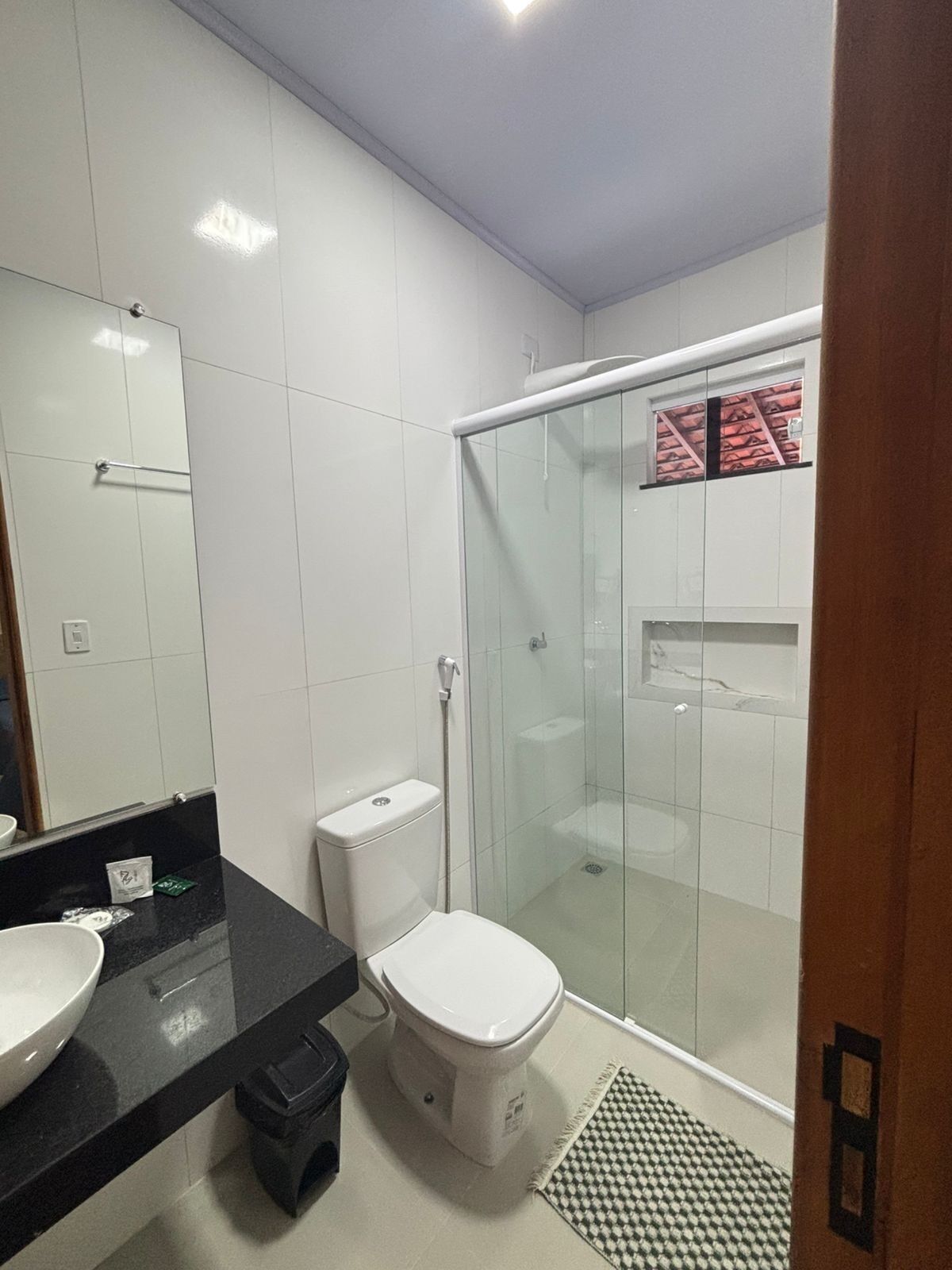 Un baño moderno con cabina de ducha de vidrio, inodoro blanco y encimera negra con lavamanos.