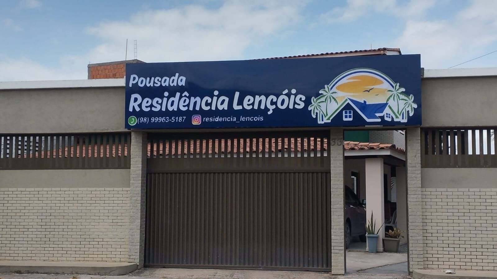 A building with a large garage door, a signboard with contact information, and a logo featuring palm trees and a house.