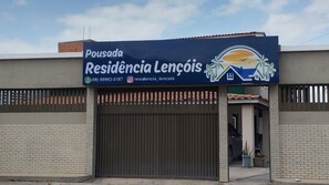 A building with a large garage door, a signboard with contact information, and a logo featuring palm trees and a house. - Pousada Residência Lençóis (Barreirinhas)