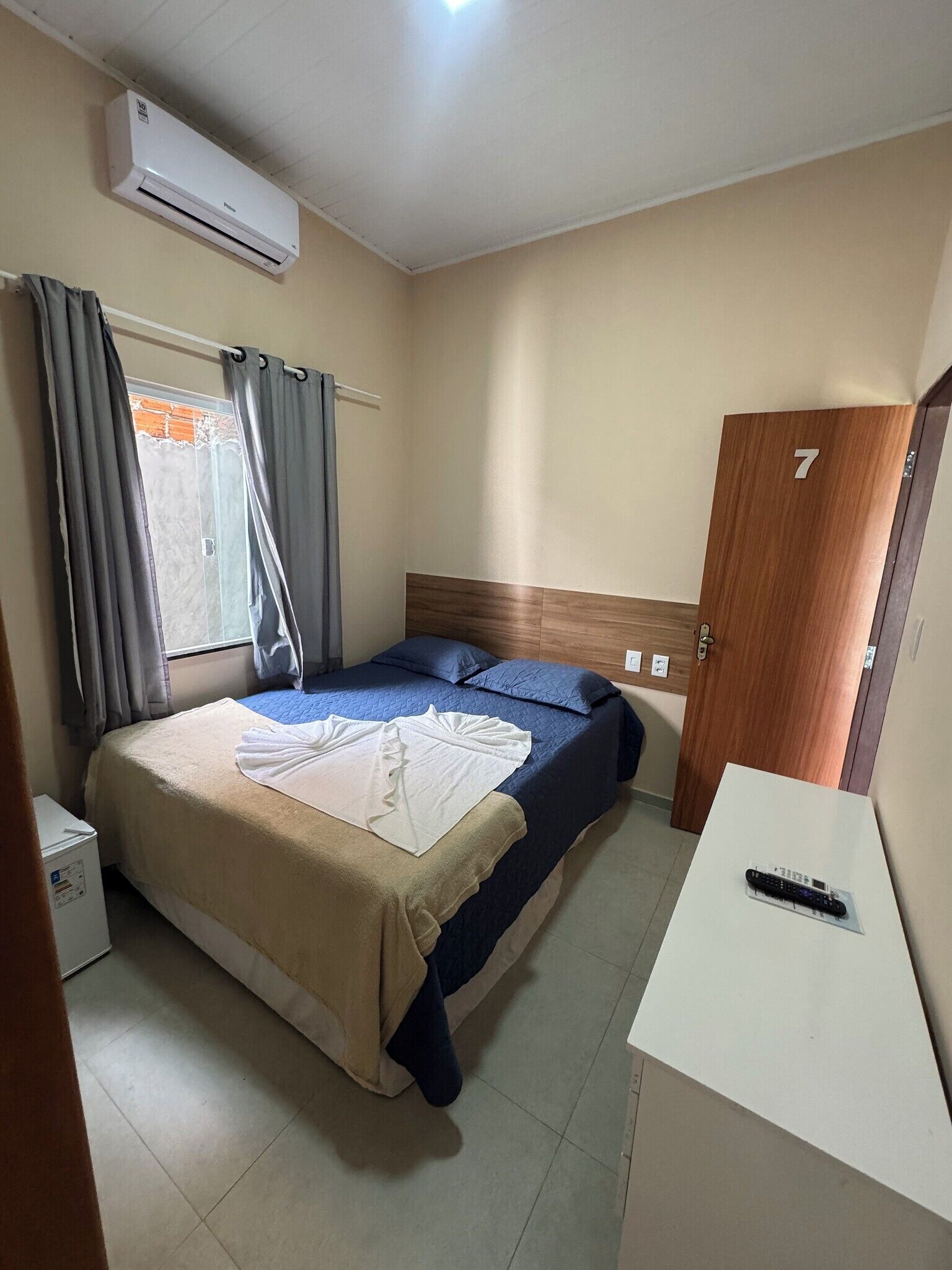 A hotel room with a bed, a desk, an air conditioning unit, a door, and a window with curtains.