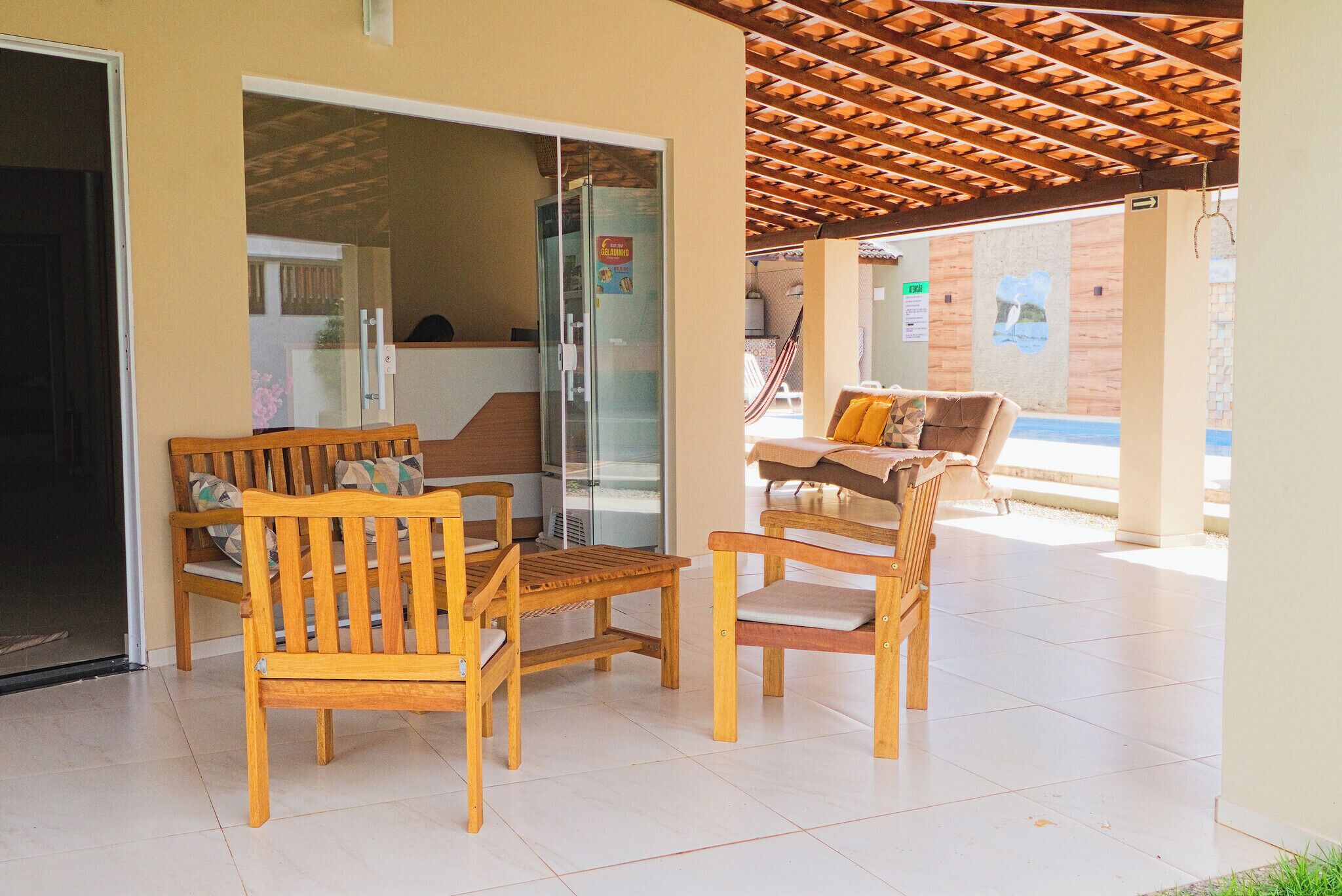 Un espacio de estar al aire libre cubierto, con mobiliario de madera, puerta de cristal y suelo de baldosas.