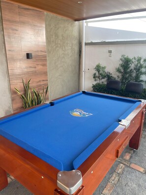 A pool table with a logo in the center, surrounded by wooden panels and a potted plant. - Pousada Residência Lençóis (Barreirinhas)