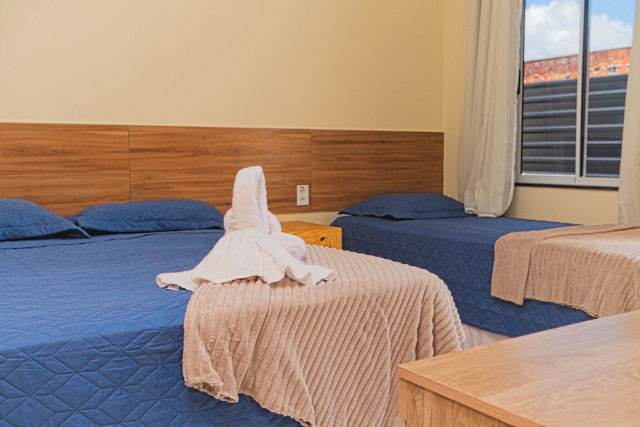 Quarto de hotel com duas camas, uma cabeceira de madeira, uma janela com cortinas e uma mesa de cabeceira de madeira.