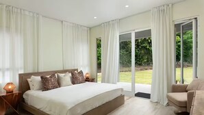 Ein Schlafzimmer mit einem großen Bett, zwei Nachttischen, einem Sessel und einer Glastür, die in einen Garten führt.