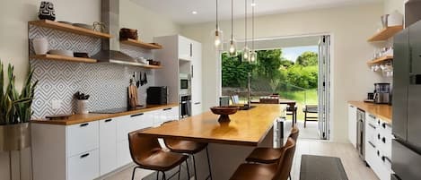 A modern kitchen with a central island, bar stools, built-in shelves, and a view to the outdoors.