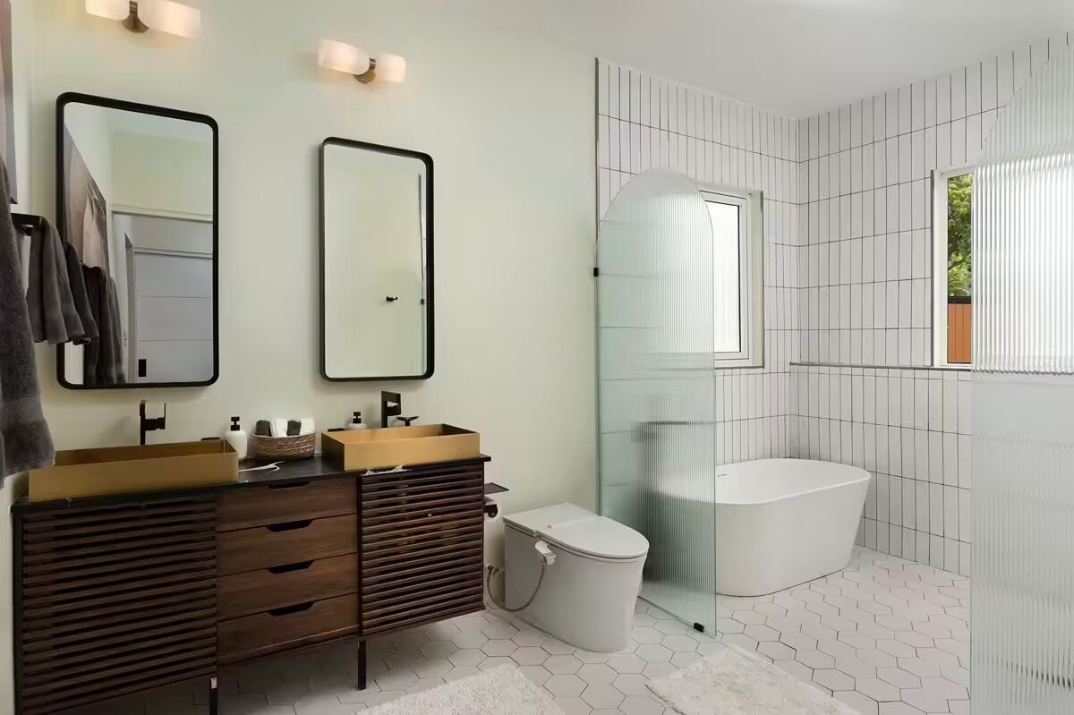 A modern bathroom with a vanity, two mirrors, a bathtub, and a shower enclosure.