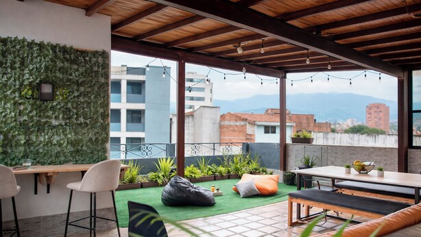 An outdoor patio with a wooden ceiling, a bar area, seating, and a view of buildings and mountains. - 302-3 habitacion con baño privado en Coliving con terraza (Medellín)