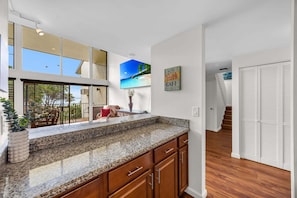 A modern kitchen with granite countertops, wooden cabinets, and a large window overlooking a patio. - Maalaea Oceanview 1BD + Loft Getaway (Wailuku)