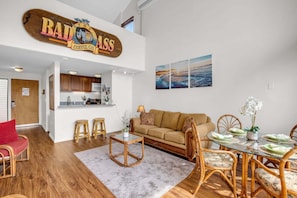 A modern living space with a kitchen, a dining area with a glass table, and a sofa. - Maalaea Oceanview 1BD + Loft Getaway (Wailuku)