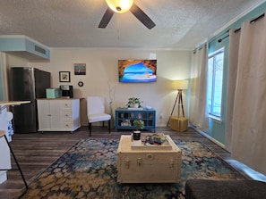 Ein Wohnzimmer mit einem blauen Schrank, einem weißen Sessel, einem blauen Sofa, einem Koffer und einem Fernseher an der Wand.