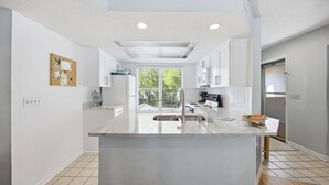 Una cocina moderna con una isla central, armarios blancos y un ventanal grande.