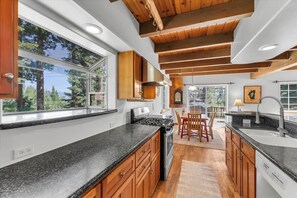 Eine moderne Küche mit Granitarbeitsplatten, Holzschränken und einem großen Fenster mit Blick auf einen Wald.