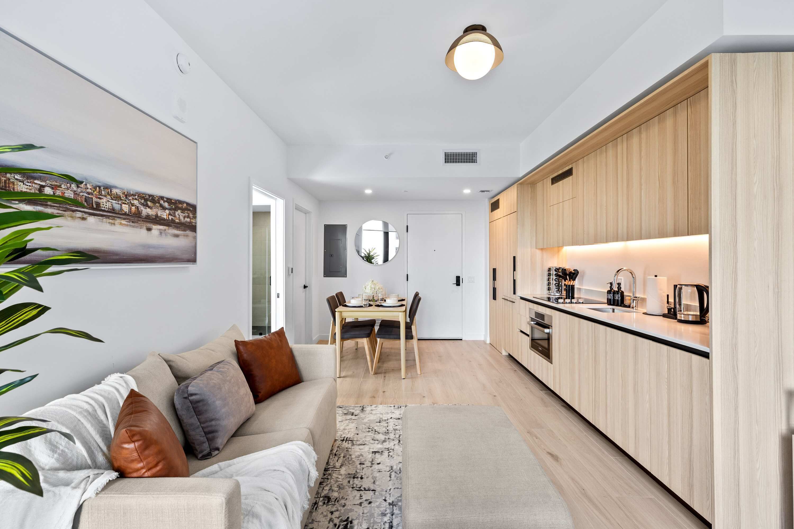 Una cucina moderna con mobili in legno, una zona pranzo con tavolo e sedie, e un soggiorno con divano e cuscini.