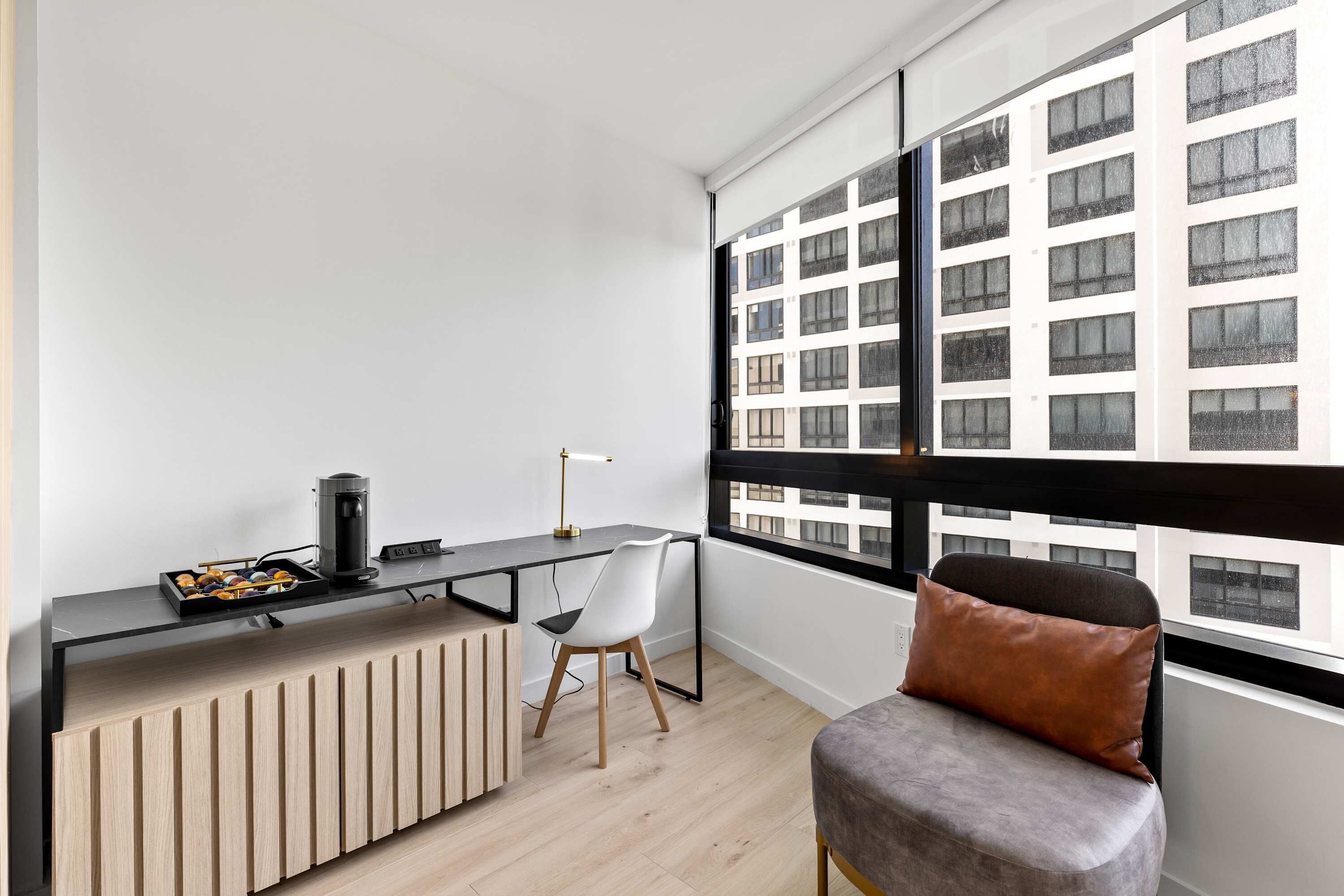 A modern room with a desk, chair, and a view of a building through large windows.