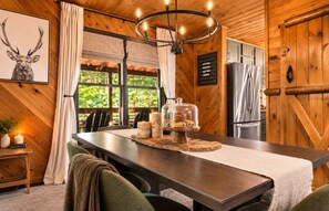 A wooden interior with a dining table, chairs, a chandelier, a refrigerator, and a window with a view of greenery. - Blue Ridge Cabin Sleeps 12: Games, Views, Hot Tub (Blue Ridge)
