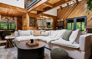 Ein gemütliches Wohnzimmer mit einem großen Ecksofa, einem runden Couchtisch und Blick auf die Küche und den Essbereich.