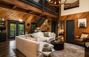 Ein großzügiges Wohnzimmer mit hohen Decken, Holzbalken, einer großen Sofagarnitur, einem Couchtisch und einem Kamin.