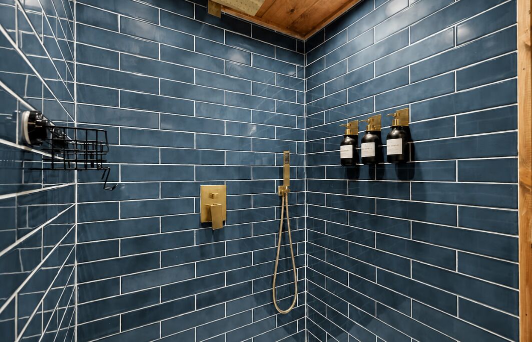 A shower area with blue-tiled walls, a gold showerhead, and three bottles of shampoo.