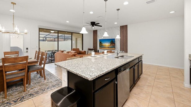 A modern kitchen with granite countertops, a black island, and a dining area with wooden chairs and a table. - Group Hub Near Disney | 4BR with Pool and BBQ | Windsor of Westside Resort (Four Corners)