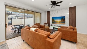 A modern living room with a sofa set, a dining table, and a large TV. - Group Hub Near Disney | 4BR with Pool and BBQ | Windsor of Westside Resort (Four Corners)