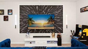 A living room with a large TV, Star Wars memorabilia, and a blue sofa. - Group Hub Near Disney | 4BR with Pool and BBQ | Windsor of Westside Resort (Four Corners)