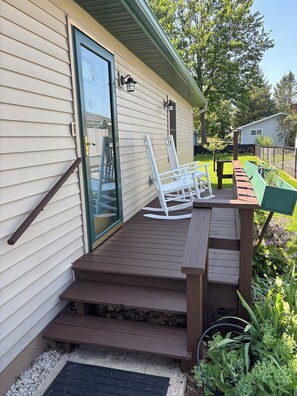 A wooden deck with a bench and chairs, a door, and a small garden area with plants. - Houghton lake 2 bedroom 2 bath ranch in Prudenville - perfect relaxing getaways… (Prudenville)