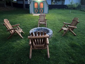 A backyard with a fire pit, wooden chairs, and a shed.