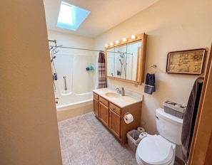 Une salle de bain Ă©quipĂ©e dâune baignoire, dâun meuble-lavabo, de toilettes et dâune lucarne.