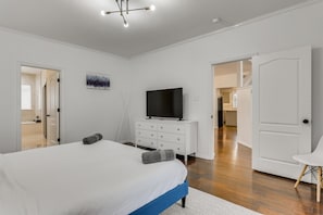 Une chambre à coucher avec un grand lit, un téléviseur posé sur une commode et une porte donnant sur une autre pièce.