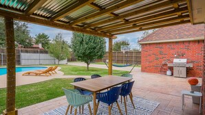Eine überdachte Terrasse mit Tisch und Stühlen, ein Schwimmbad und ein Barbereich.