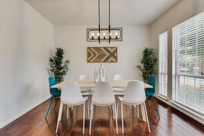 A dining area with a wooden table, white chairs, a pendant light, and two potted plants.