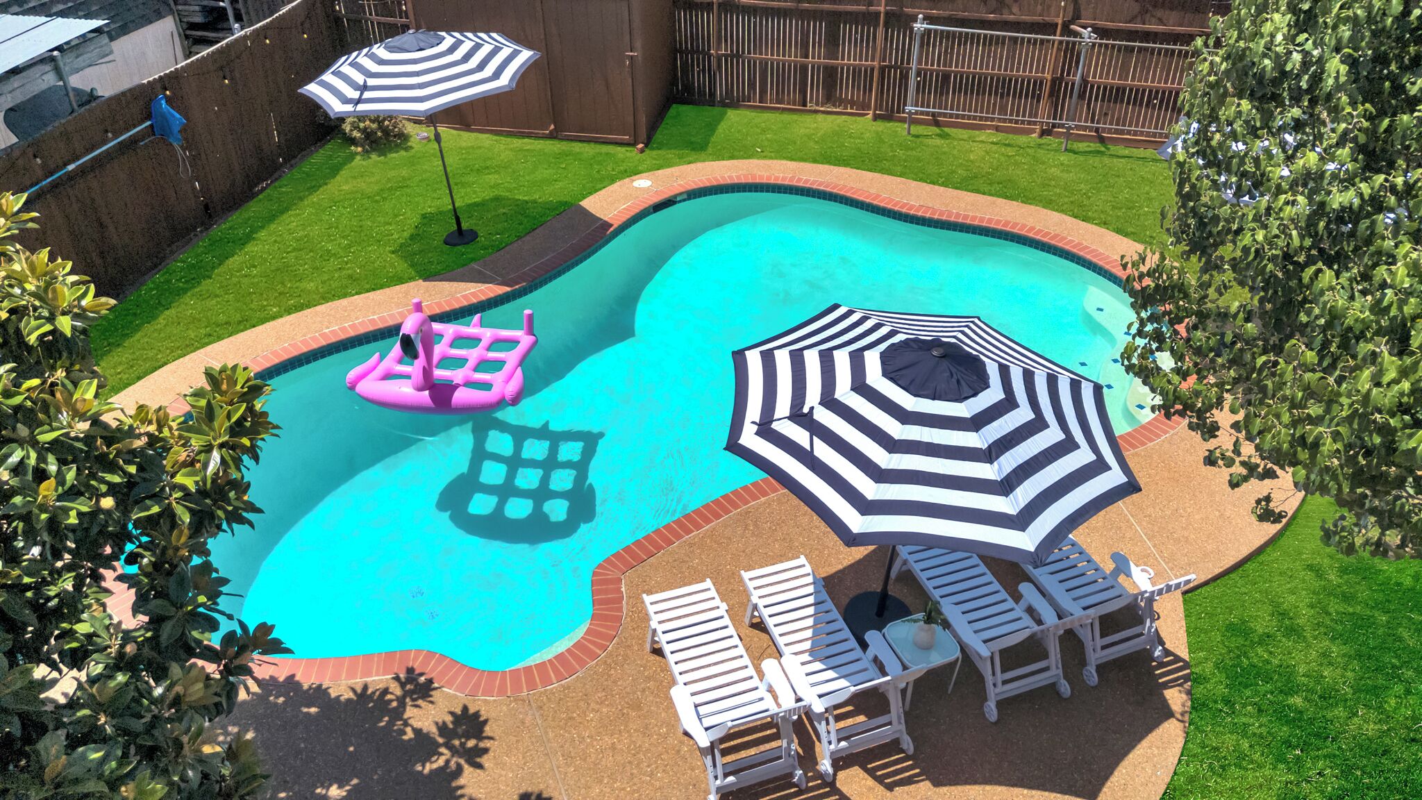 A backyard with a swimming pool, two lounge chairs, and two umbrellas.