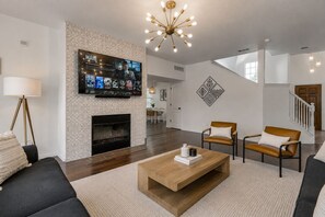 Una sala de estar moderna con chimenea, televisor montado en la pared y una escalera que sube a un nivel superior.