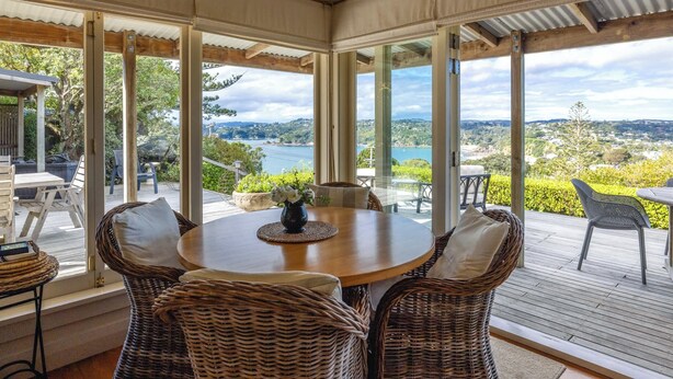 Un espacio de comedor al aire libre con techo, mobiliario de mimbre, una mesa redonda y vistas a un lago y colinas.