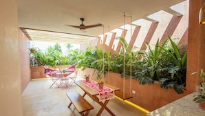A patio with a wooden table and benches, surrounded by lush greenery and a ceiling fan. - El Canario, double room with garden in Casa Sofia Center (Mérida)