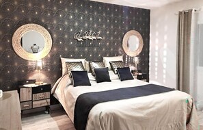 A bedroom with a bed, two bedside tables, a mirror, and a wall with a textured pattern. - Maison avec piscine privée (Marguerittes)