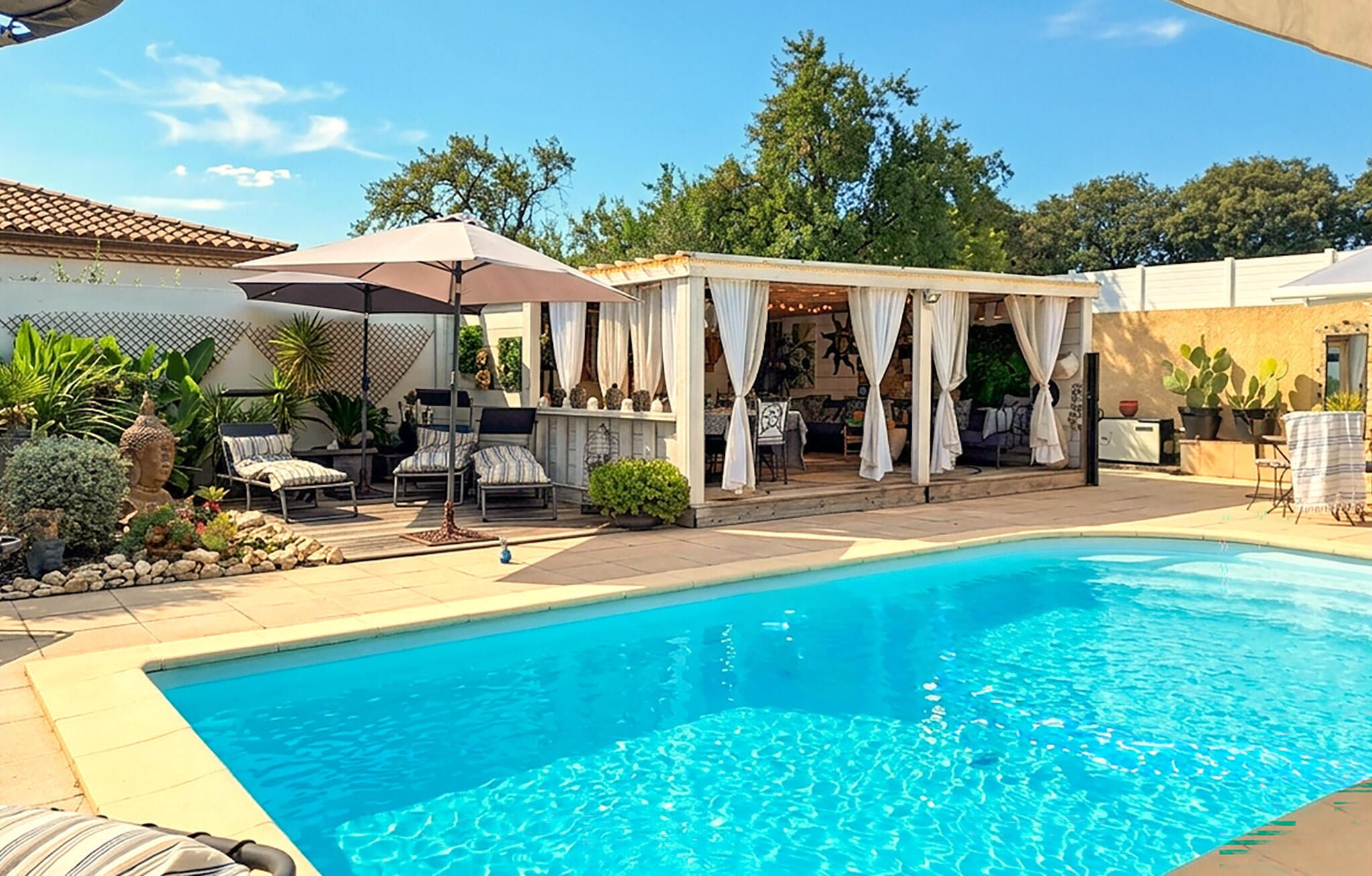 Une piscine dotée d’un patio couvert, de chaises longues et de plantes en pot.