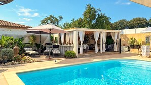 Piscina com área de estar coberta, cadeiras de descanso e plantas em vasos.